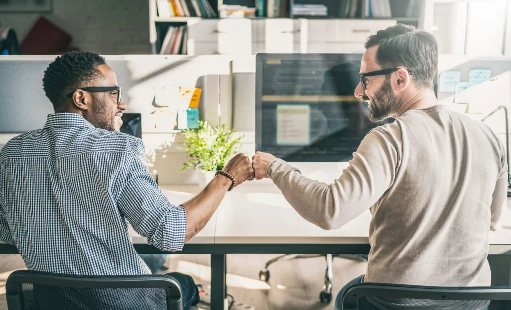 Two professionals celebrating with a fist bump in a modern office setting